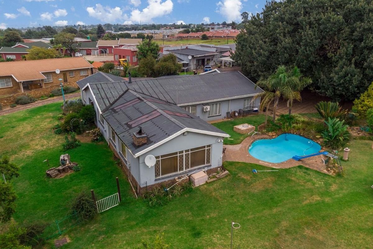 Aerial view of a small holding property featuring a residential dwelling with a metal roof, a swimming pool, and expansive garden grounds.