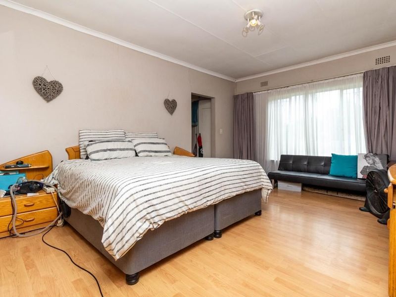 A spacious bedroom featuring laminate flooring, neutral wall tones, and large windows that provide ample natural light.