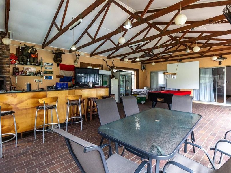 Spacious covered patio featuring a built-in bar, brick fireplace, and exposed timber trusses, ideal for outdoor entertaining and social gatherings.