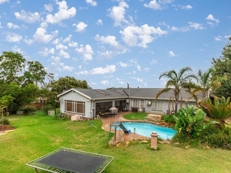 Rear view of the property featuring a swimming pool, paved patio area, and a spacious garden with established landscaping.