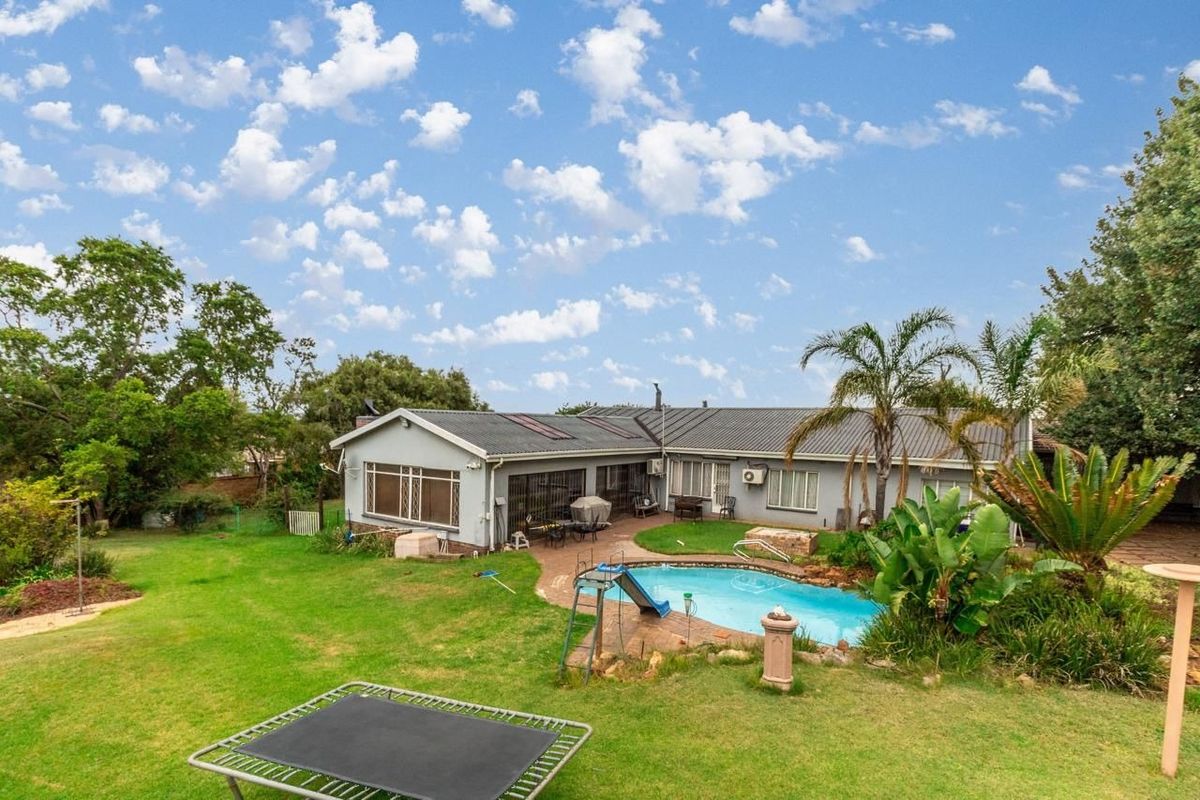 Rear view of the property featuring a swimming pool, paved patio area, and a spacious garden with established landscaping.