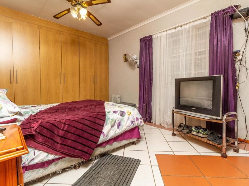 A bedroom featuring built-in wooden cupboards, tiled flooring, and a ceiling fan, with direct access to the exterior via a sliding door.
