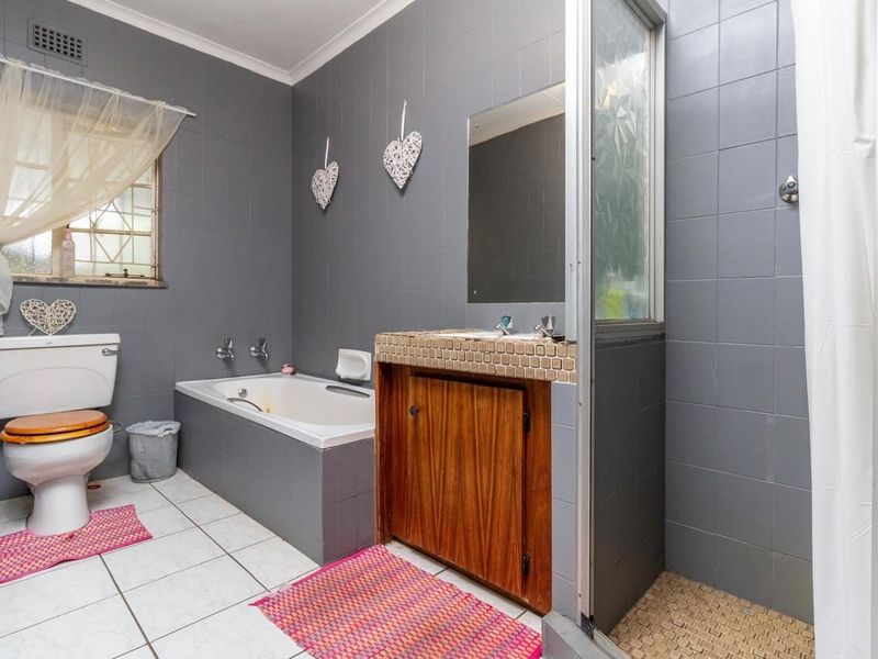 A functional bathroom featuring a built-in bathtub, a separate shower enclosure, a vanity cabinet, and a toilet with grey wall tiling.