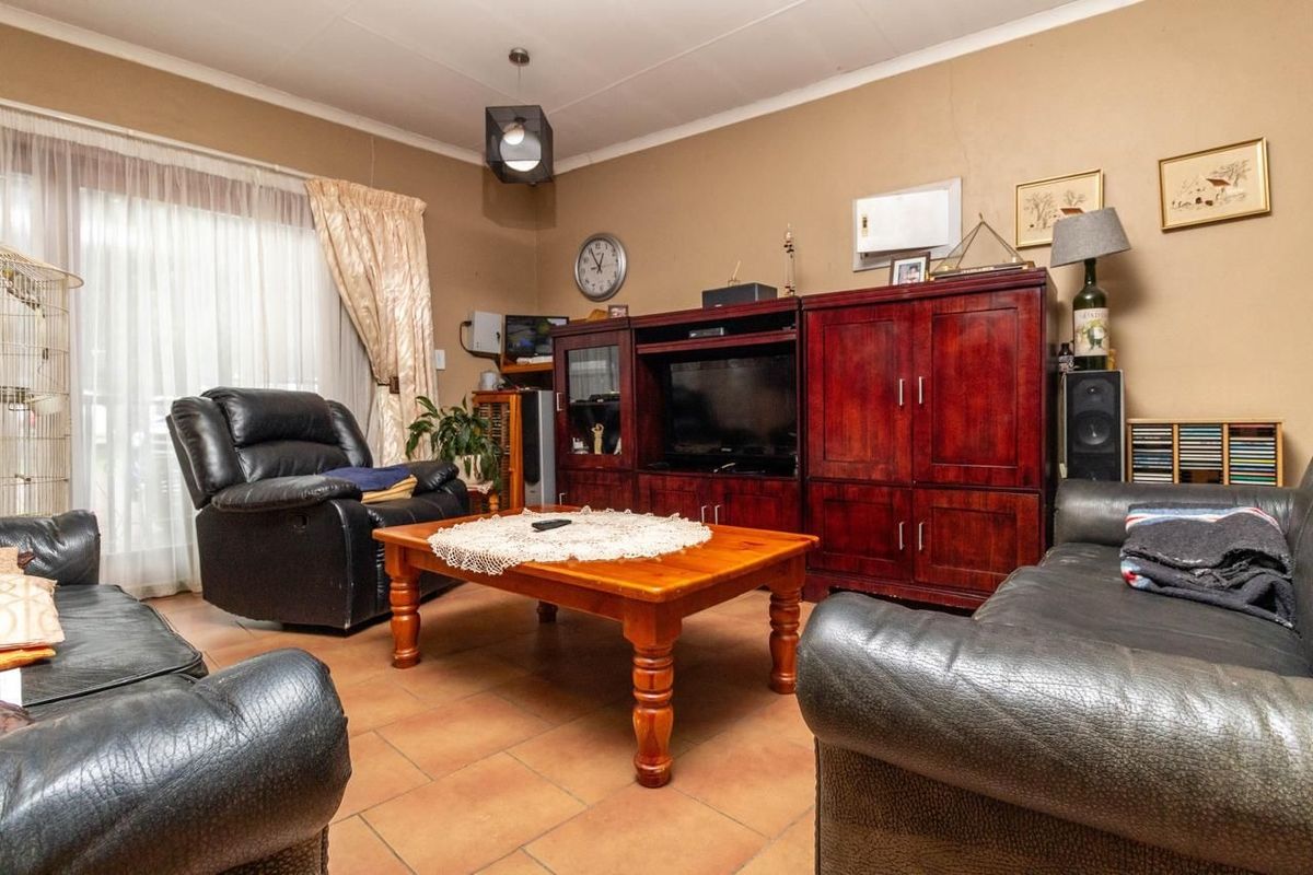 A living room featuring tiled flooring and a sliding glass door providing natural light, with visible wall plaster cracks requiring maintenance.