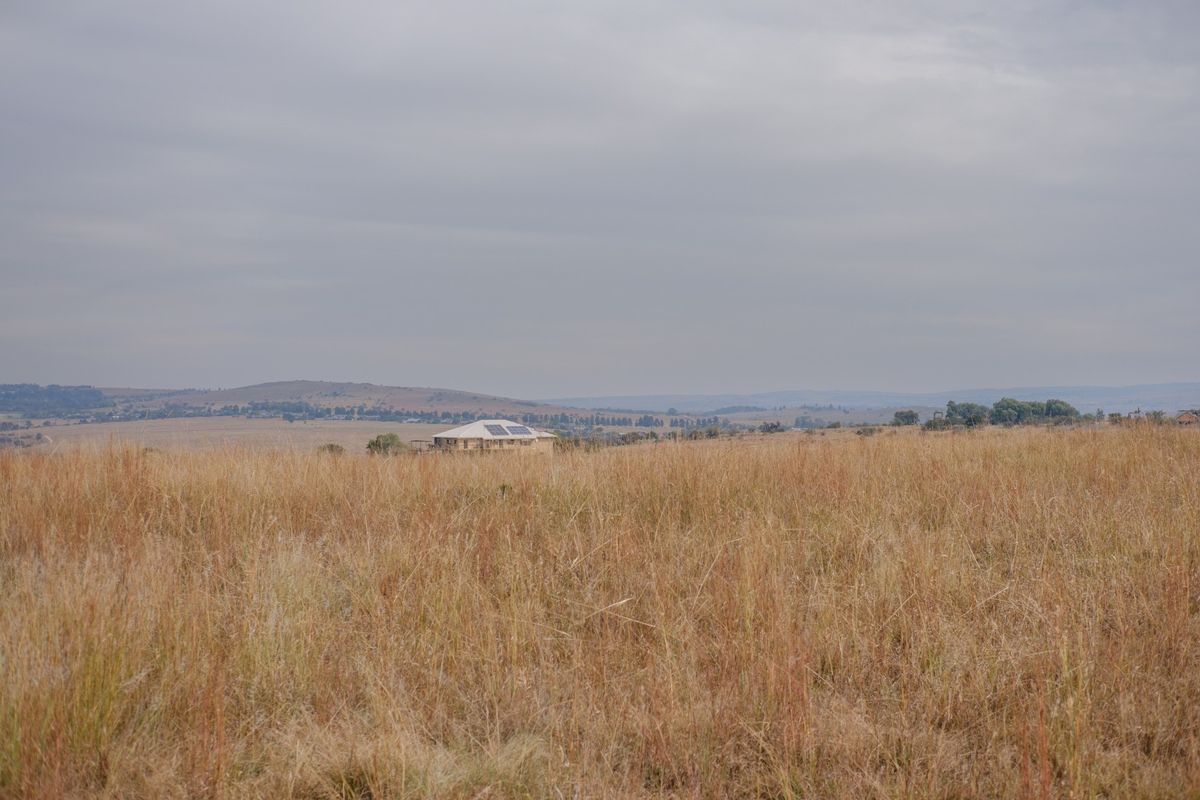 A wide-angle view of expansive open grassland with a distant residential property visible on the horizon under a cloudy sky.