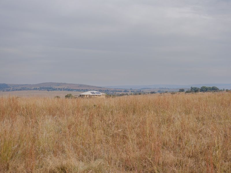 A wide-angle view of expansive open grassland with a distant residential property visible on the horizon under a cloudy sky.