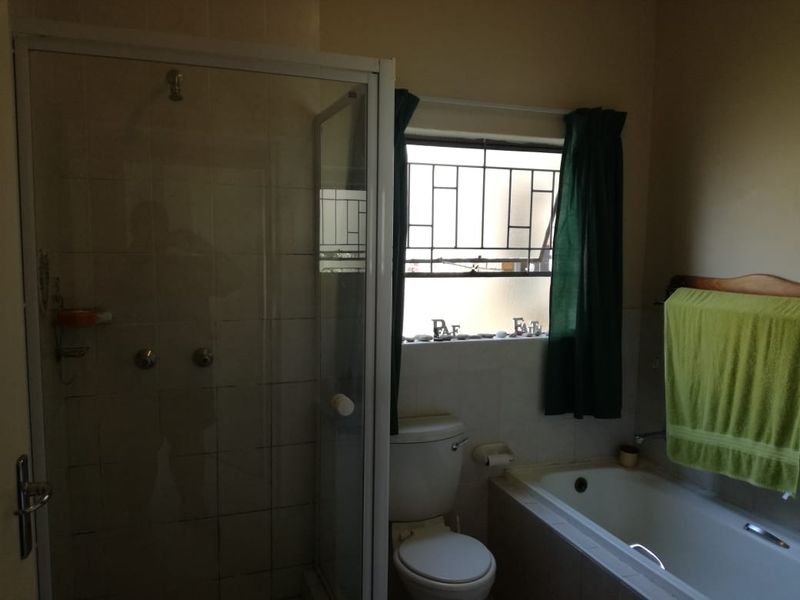 A functional bathroom featuring a separate shower enclosure, a bathtub, and a toilet, with security bars installed on the window.