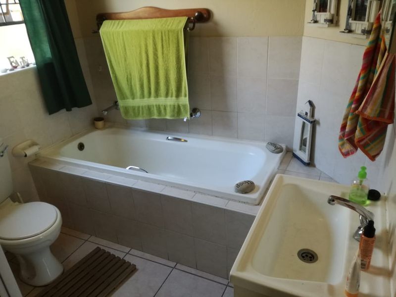 A functional bathroom featuring a built-in bathtub, pedestal washbasin, and tiled finishes, offering a standard layout with potential for modern cosmetic updates.