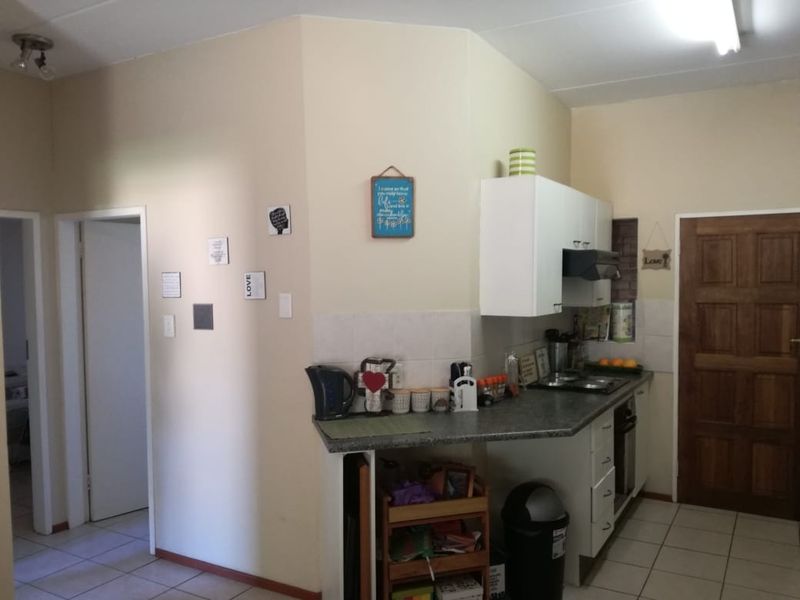 A functional kitchen area featuring built-in cabinetry, a tiled backsplash, and a hob with an extractor fan, finished with tiled flooring.