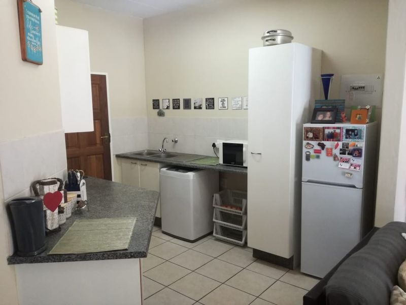 A functional kitchen featuring laminate countertops, a stainless steel sink, tiled splashbacks, and tiled flooring with ample built-in cabinetry.