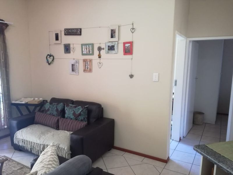 A living room area featuring tiled flooring and neutral wall finishes, providing a functional space with access to an adjacent hallway.