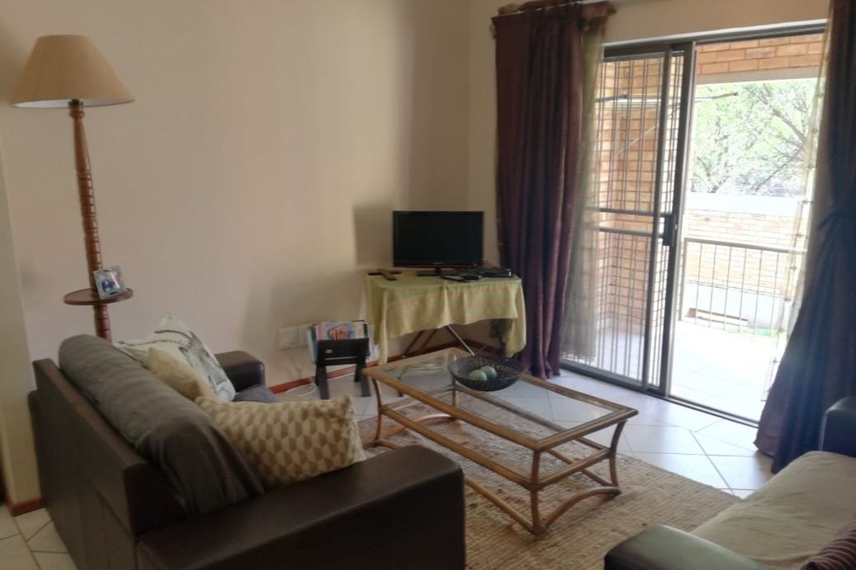 A living room featuring tiled flooring and a sliding glass door with a security gate leading to an outdoor balcony area.
