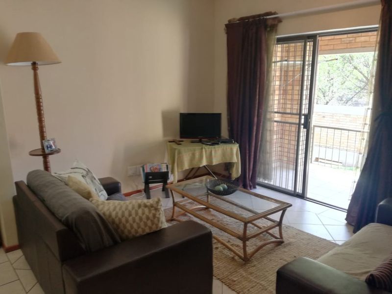 A living room featuring tiled flooring and a sliding glass door with a security gate leading to an outdoor balcony area.
