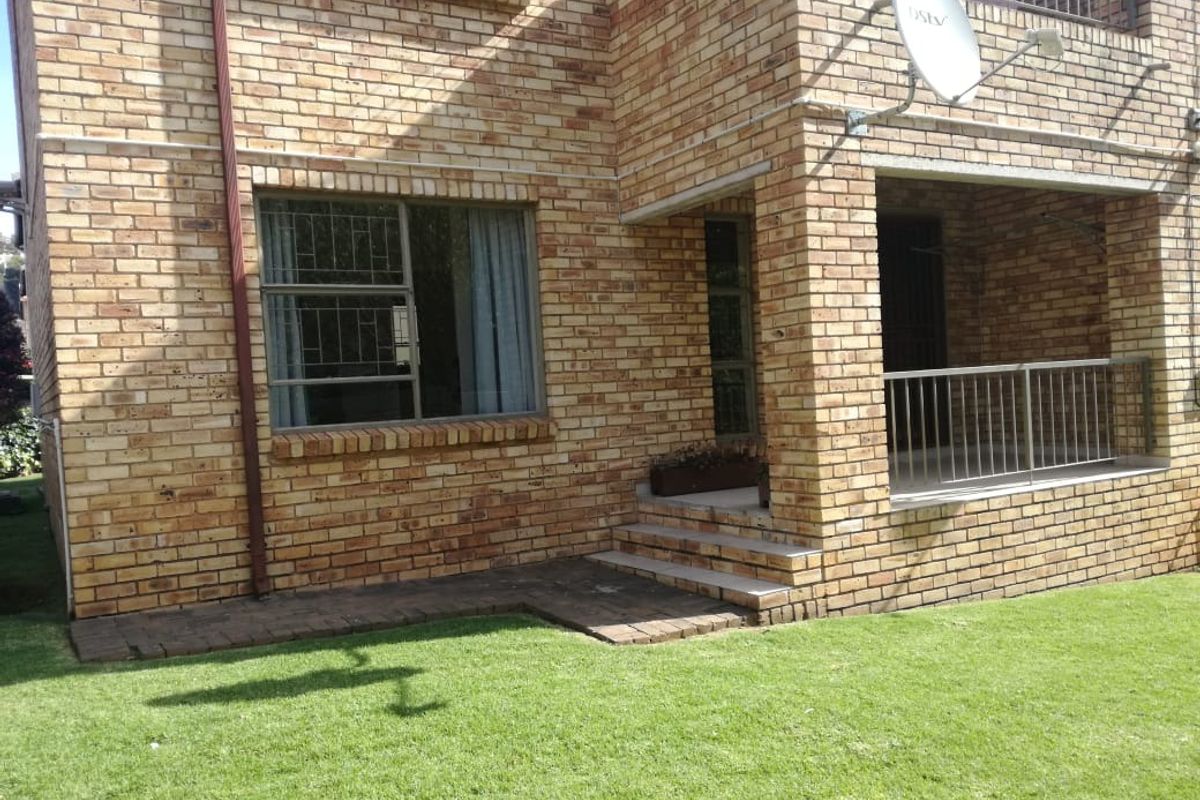 Rear view of a face brick apartment building featuring a small patio area, metal security bars on windows, and a well-maintained lawn.