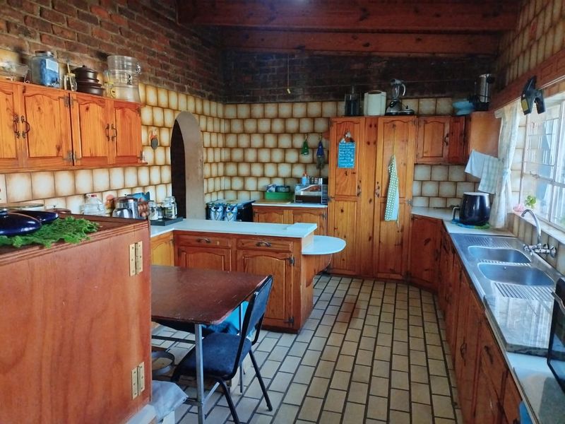 Rustic kitchen featuring exposed brick walls, timber cabinetry, exposed ceiling beams, and tiled flooring, offering a traditional aesthetic with potential for modern updates.