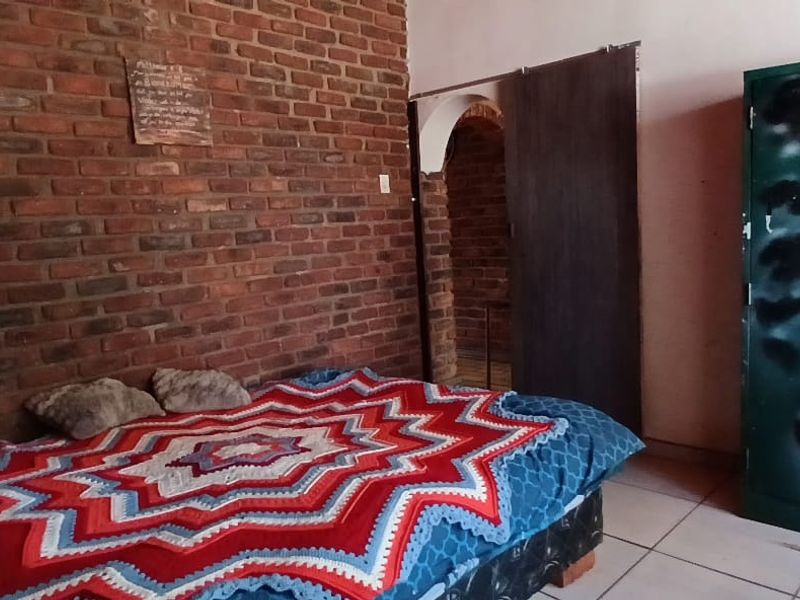 A bedroom featuring an exposed brick feature wall, tiled flooring, and a sliding door leading to an adjacent space.