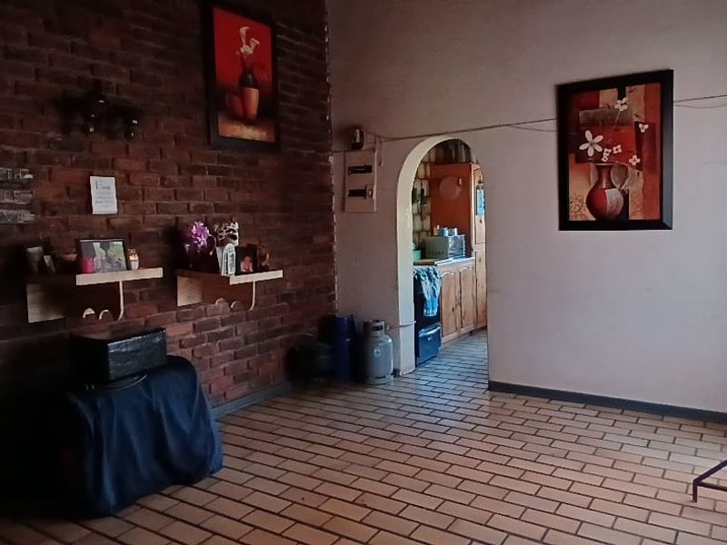 Living room featuring an exposed brick feature wall, tiled flooring, and an arched doorway leading to the kitchen area.