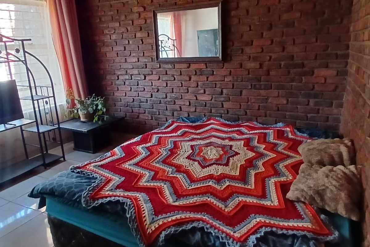 A bedroom featuring exposed brick walls and tiled flooring, providing a rustic aesthetic with natural light from a large window.