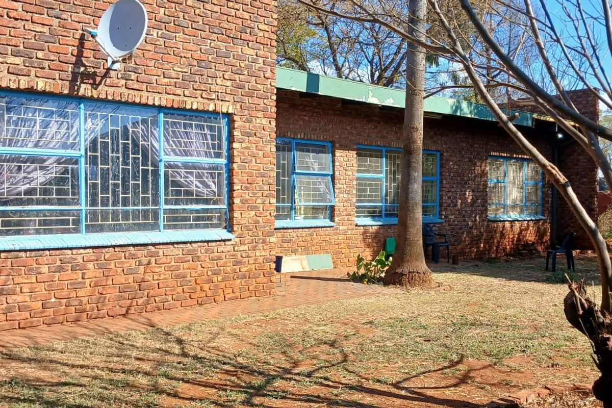 Rear view of a face brick house featuring steel-framed windows with security bars and a garden area.