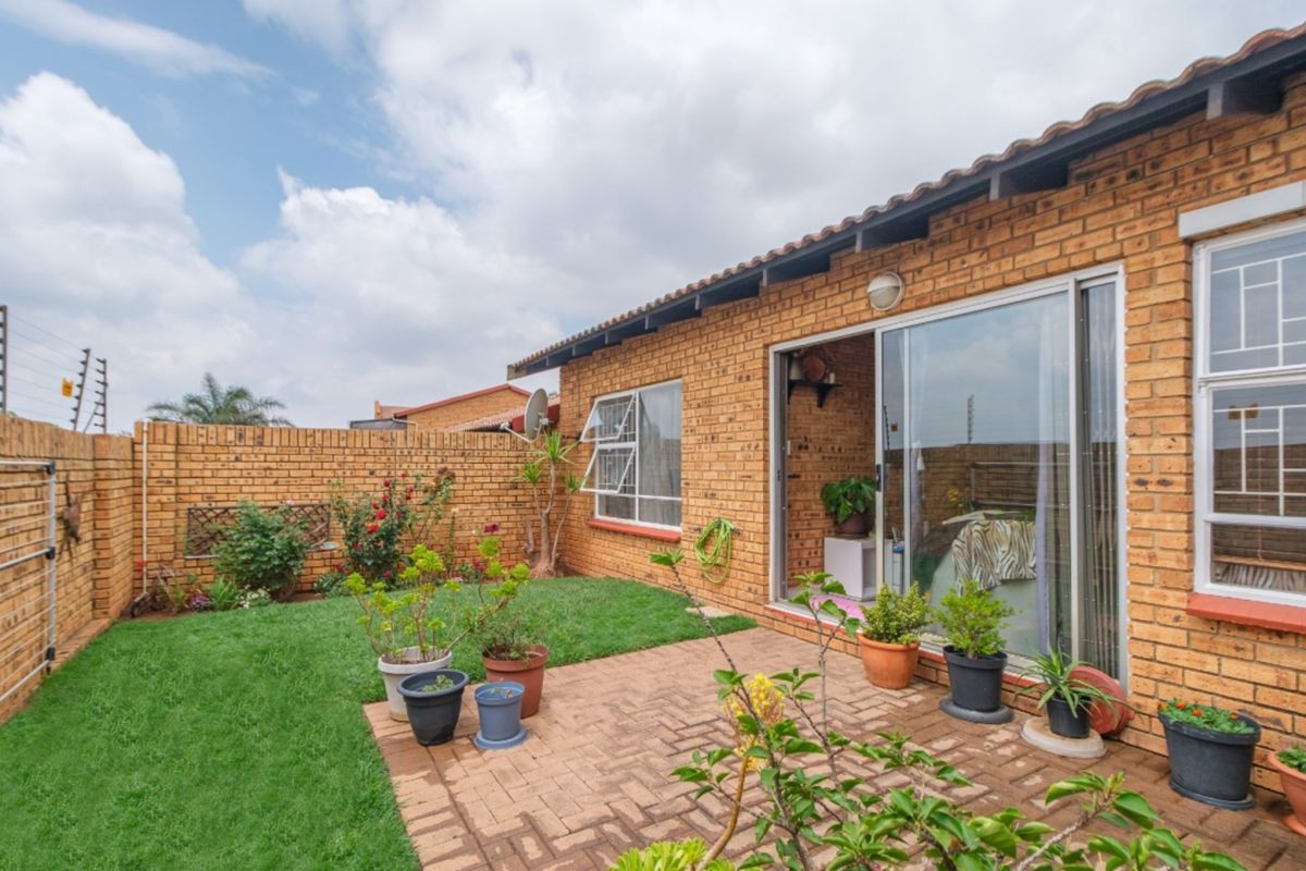 Rear exterior view of a face brick townhouse featuring a paved patio, small lawn, and secure boundary wall with electric fencing.