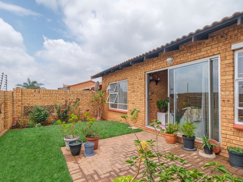 Rear exterior view of a face brick townhouse featuring a paved patio, small lawn, and secure boundary wall with electric fencing.
