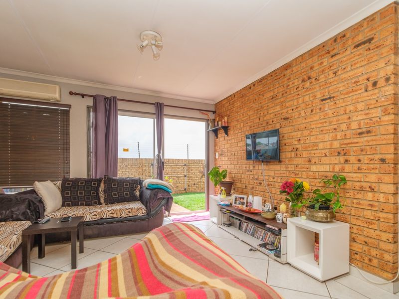 A living room featuring an exposed brick wall, tiled flooring, and a sliding glass door providing access to the rear garden area.
