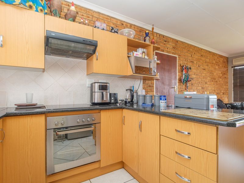 A functional kitchen featuring light wood laminate cabinetry, granite countertops, a built-in oven with hob, and a distinctive exposed brick feature wall.
