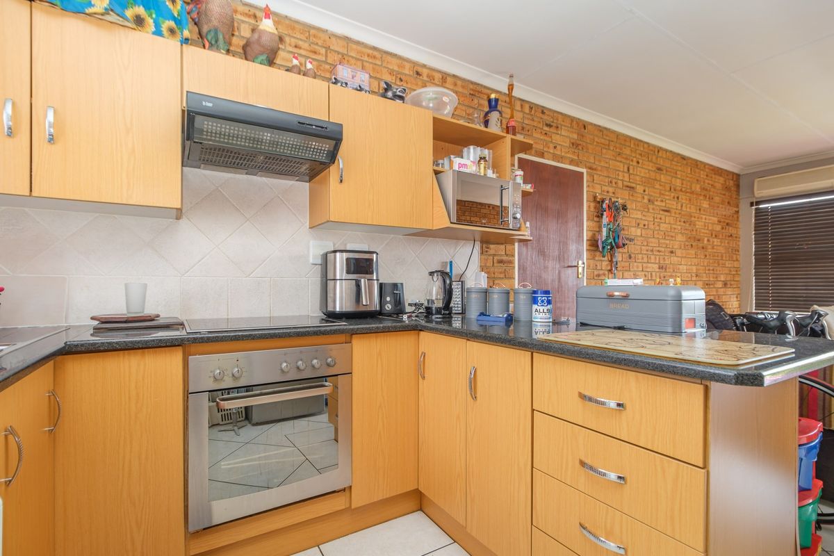 A functional kitchen featuring light wood laminate cabinetry, granite countertops, a built-in oven with hob, and a distinctive exposed brick feature wall.
