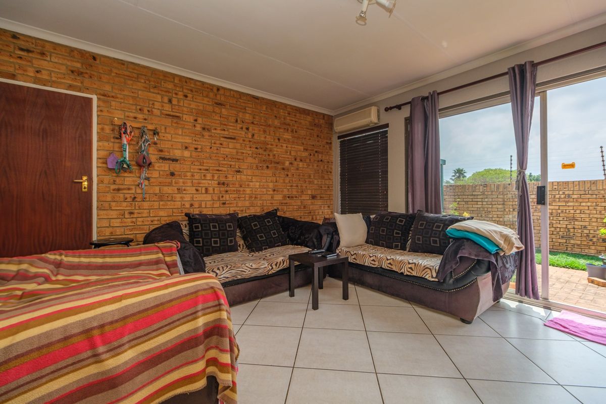 Living room featuring an exposed brick feature wall, tiled flooring, and a sliding glass door providing access to the outdoor patio area.