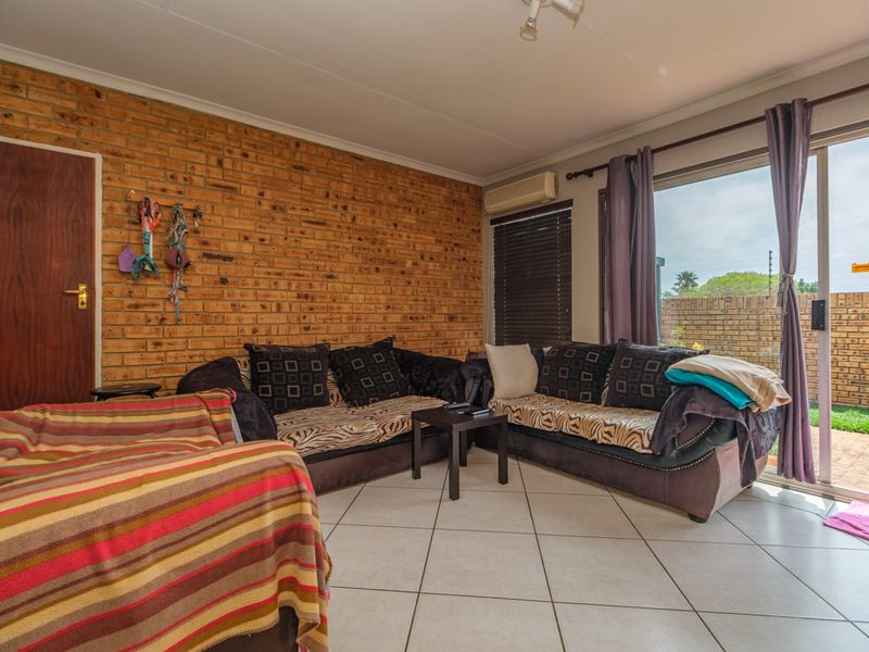 Living room featuring an exposed brick feature wall, tiled flooring, and a sliding glass door providing access to the outdoor patio area.