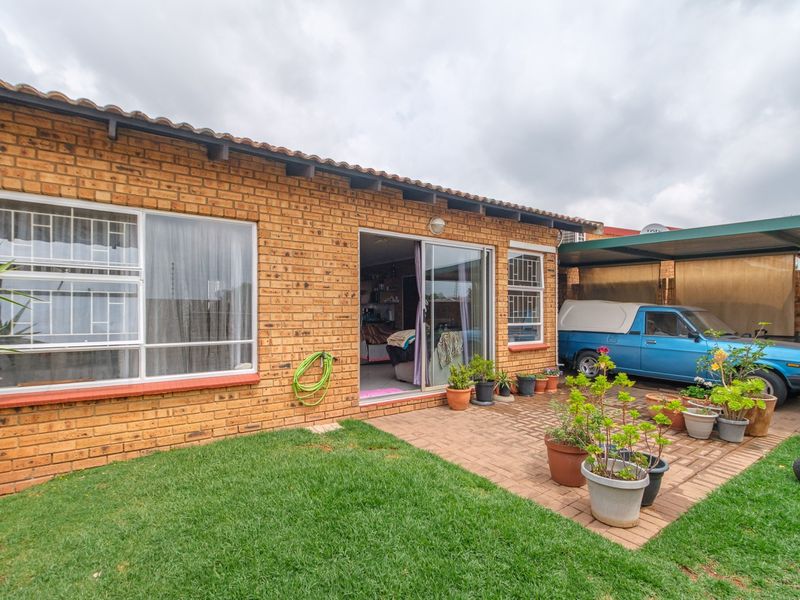 Rear view of the townhouse featuring a brick facade, a paved patio area, and an attached carport.