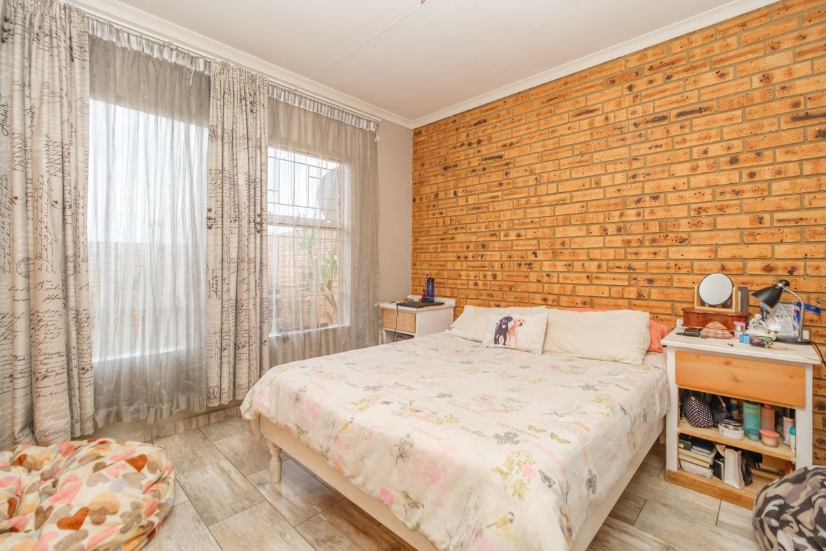 A bedroom featuring an exposed brick accent wall, tiled flooring, and large windows with security bars, offering a functional and well-lit living space.