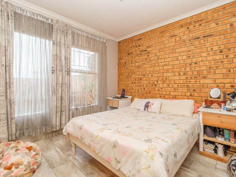 A bedroom featuring an exposed brick accent wall, tiled flooring, and large windows with security bars, offering a functional and well-lit living space.