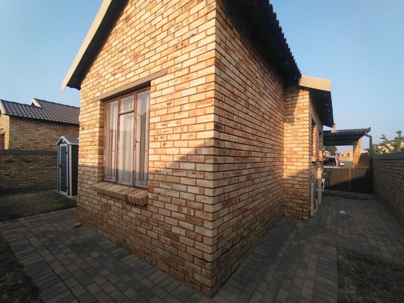 A view of the rear exterior of the face brick house, featuring a paved patio area and secure window fittings.