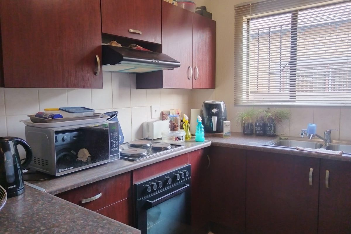 A functional kitchen featuring dark wood-veneer cabinetry, laminate countertops, a built-in oven with electric hob, and a stainless steel sink.