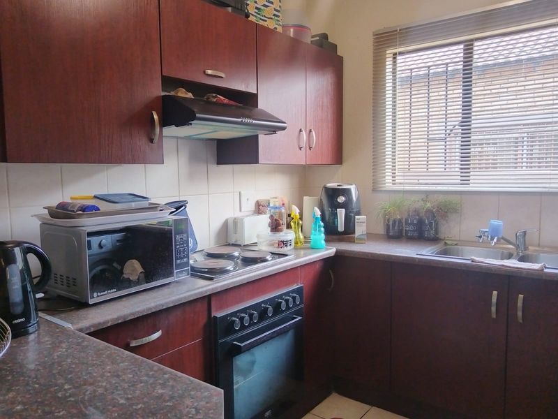 A functional kitchen featuring dark wood-veneer cabinetry, laminate countertops, a built-in oven with electric hob, and a stainless steel sink.