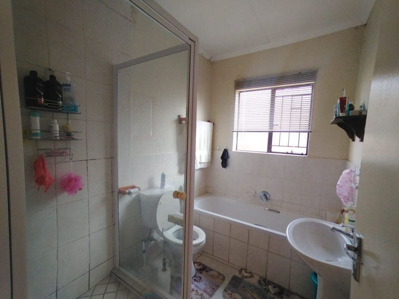 A functional bathroom featuring a shower enclosure, bathtub, pedestal basin, and toilet, with tiled finishes throughout. The space would benefit from cosmetic updates.