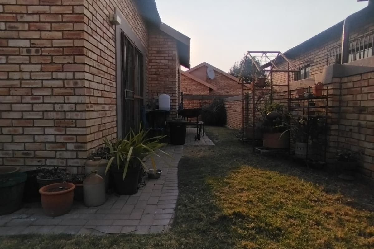 A view of the rear exterior of the property featuring a face brick facade, paved walkway, and a small lawn area.
