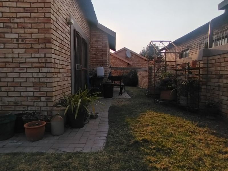 A view of the rear exterior of the property featuring a face brick facade, paved walkway, and a small lawn area.