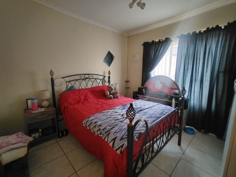 A standard bedroom featuring tiled flooring, coved ceilings, and a window fitted with security bars.
