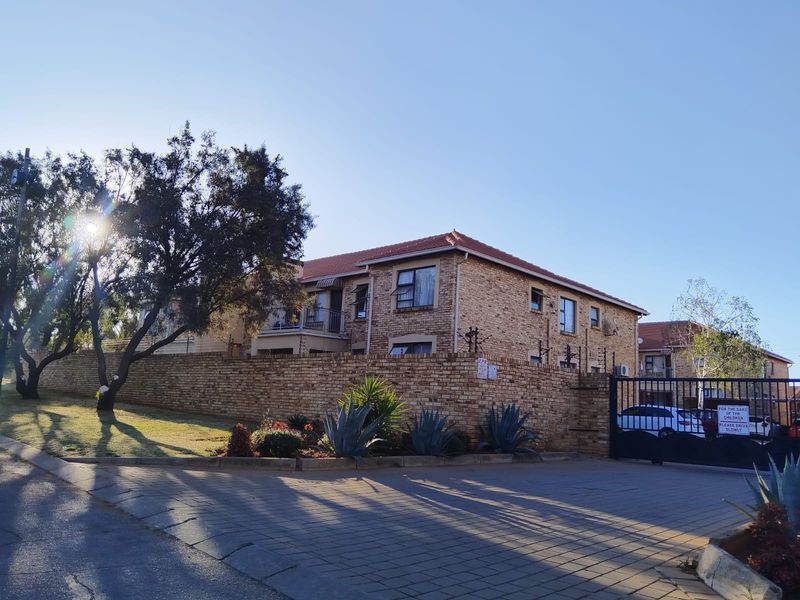 Exterior view of a face brick apartment complex featuring a secure gated entrance, paved driveway, and balconies.