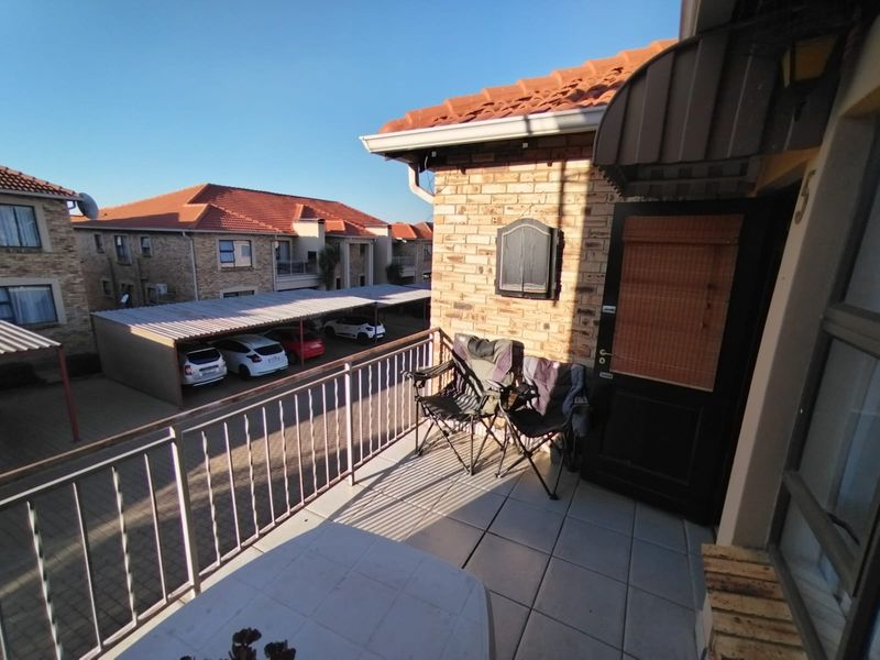 A private balcony featuring tiled flooring and a metal balustrade, overlooking the apartment complex parking area.