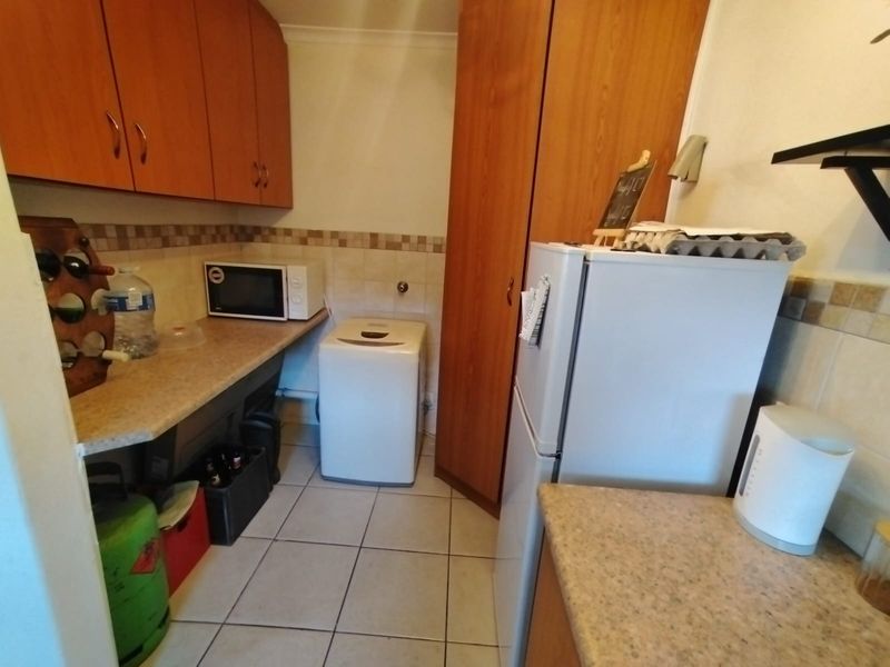A functional laundry area featuring laminate cabinetry, tiled backsplash, and durable ceramic floor tiles with dedicated space for appliances.