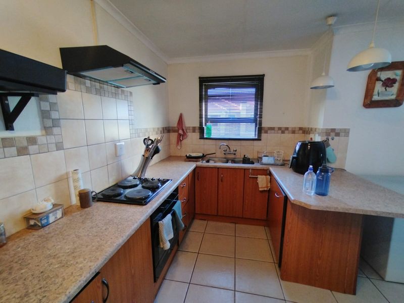 A functional U-shaped kitchen featuring wooden cabinetry, laminate countertops, a built-in oven with hob, and tiled flooring.