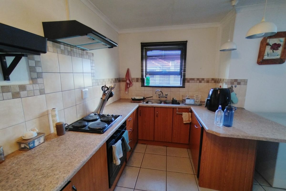 A functional U-shaped kitchen featuring wooden cabinetry, laminate countertops, a built-in oven with hob, and tiled flooring.