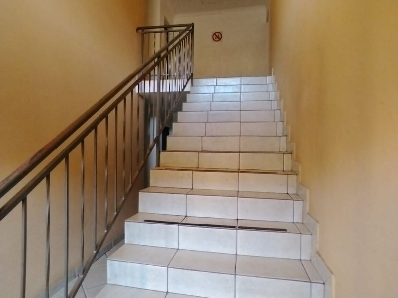 A functional interior staircase featuring tiled steps with non-slip treads and a metal handrail, providing access between levels in the apartment building.
