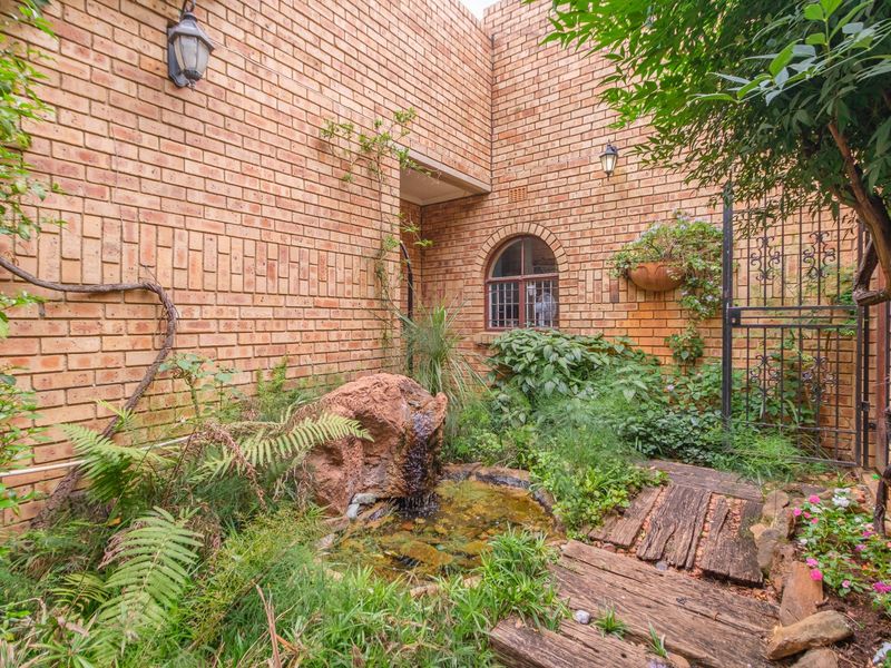 A charming courtyard garden featuring a natural stone water feature, brick walls, an arched window, and a wrought iron gate.