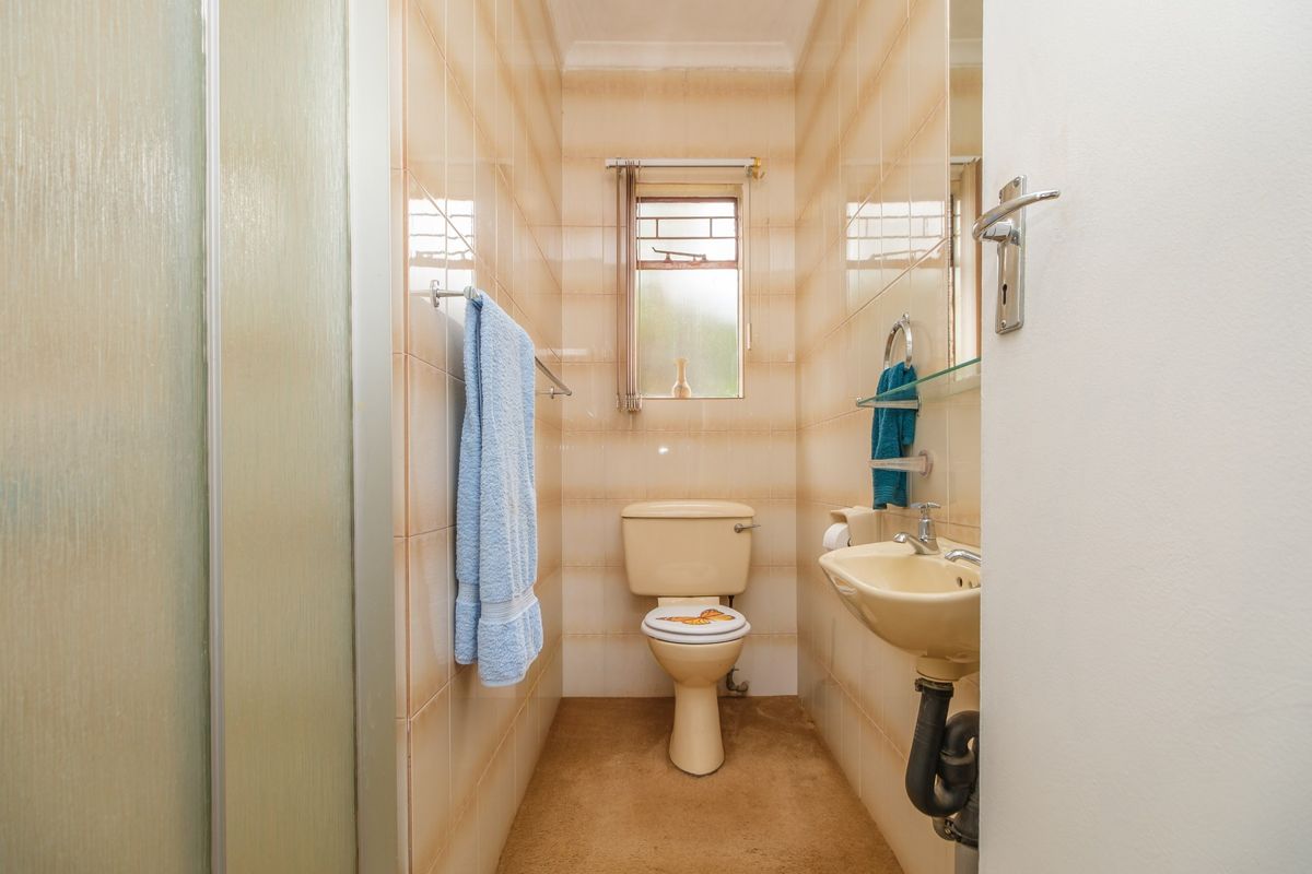 A compact bathroom featuring a shower enclosure, wall-mounted basin, and toilet with dated beige sanitaryware and wall tiling.