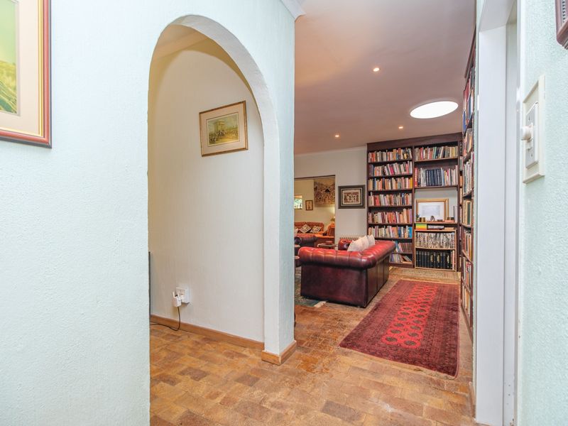A hallway featuring a distinctive arched entryway, built-in floor-to-ceiling bookshelves, and a skylight, leading into the main living area.
