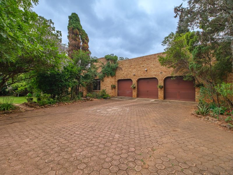 Front exterior view of a brick house featuring a triple garage with roller shutter doors and a paved driveway surrounded by mature garden landscaping.